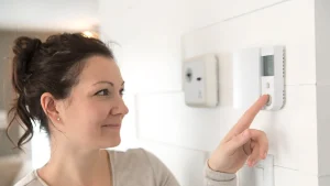 Happy lady looking at air conditioner thermostat. Smart Thermostat tips for Perth homes.