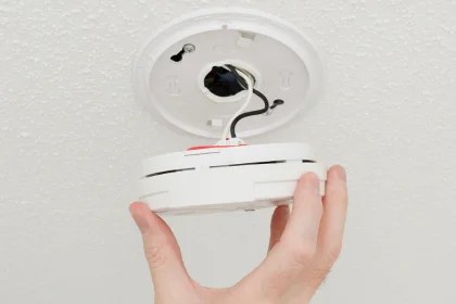 Hand of electrician installing wired smoke alarm into ceiling for COYCO