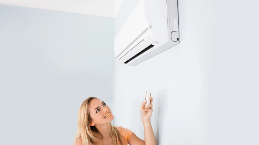 Woman holding remote to turn on split air conditioning unit for what you need to know